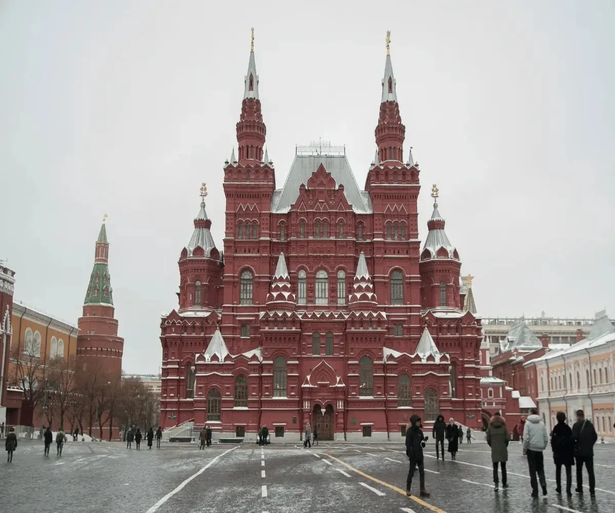 Winter view of the State Historical Museum at Red Square in Moscow, with snow-covered architecture and people walking in front.