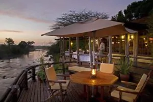 Outdoor riverside dining area at Mara Explorer Camp in Masai Mara at sunset.